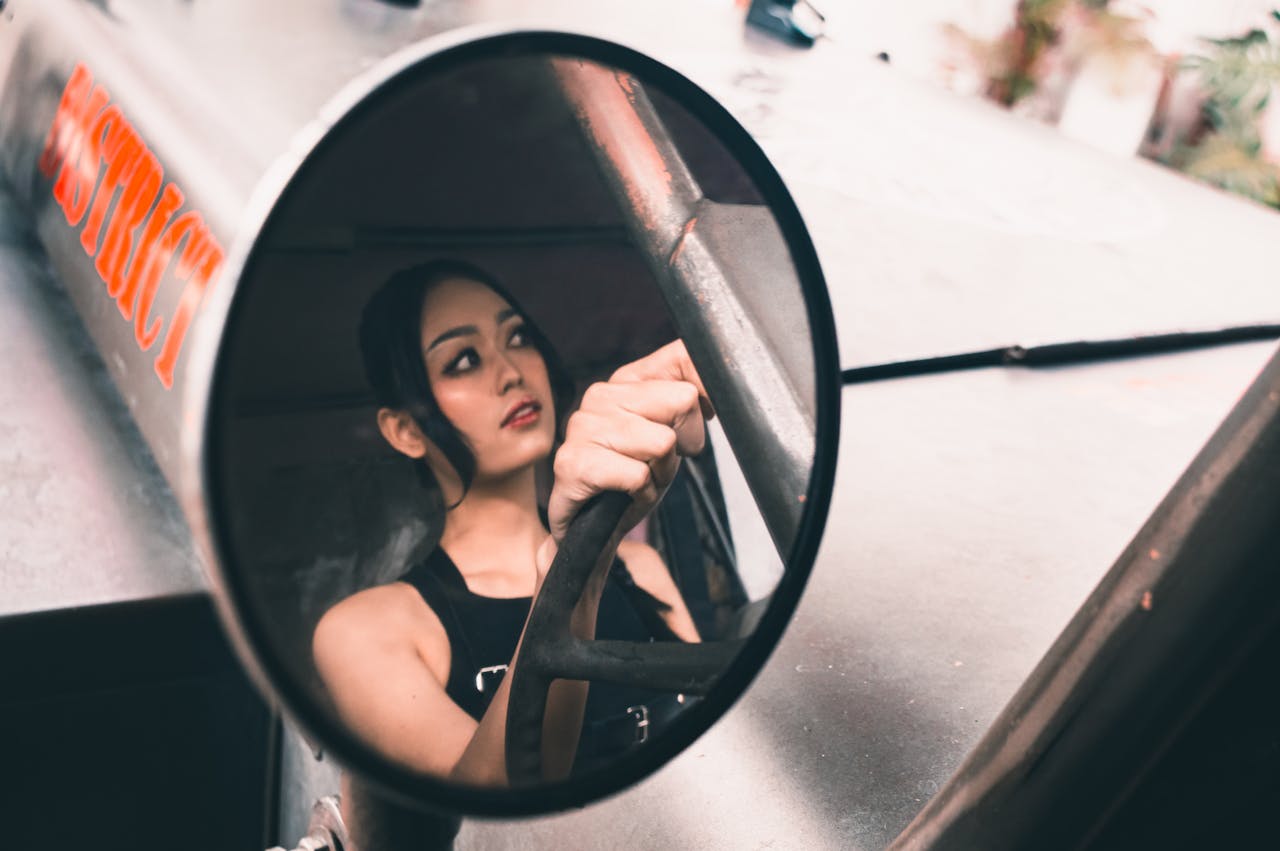 Artistic shot capturing a woman in a vehicle mirror reflection, focusing on driving.